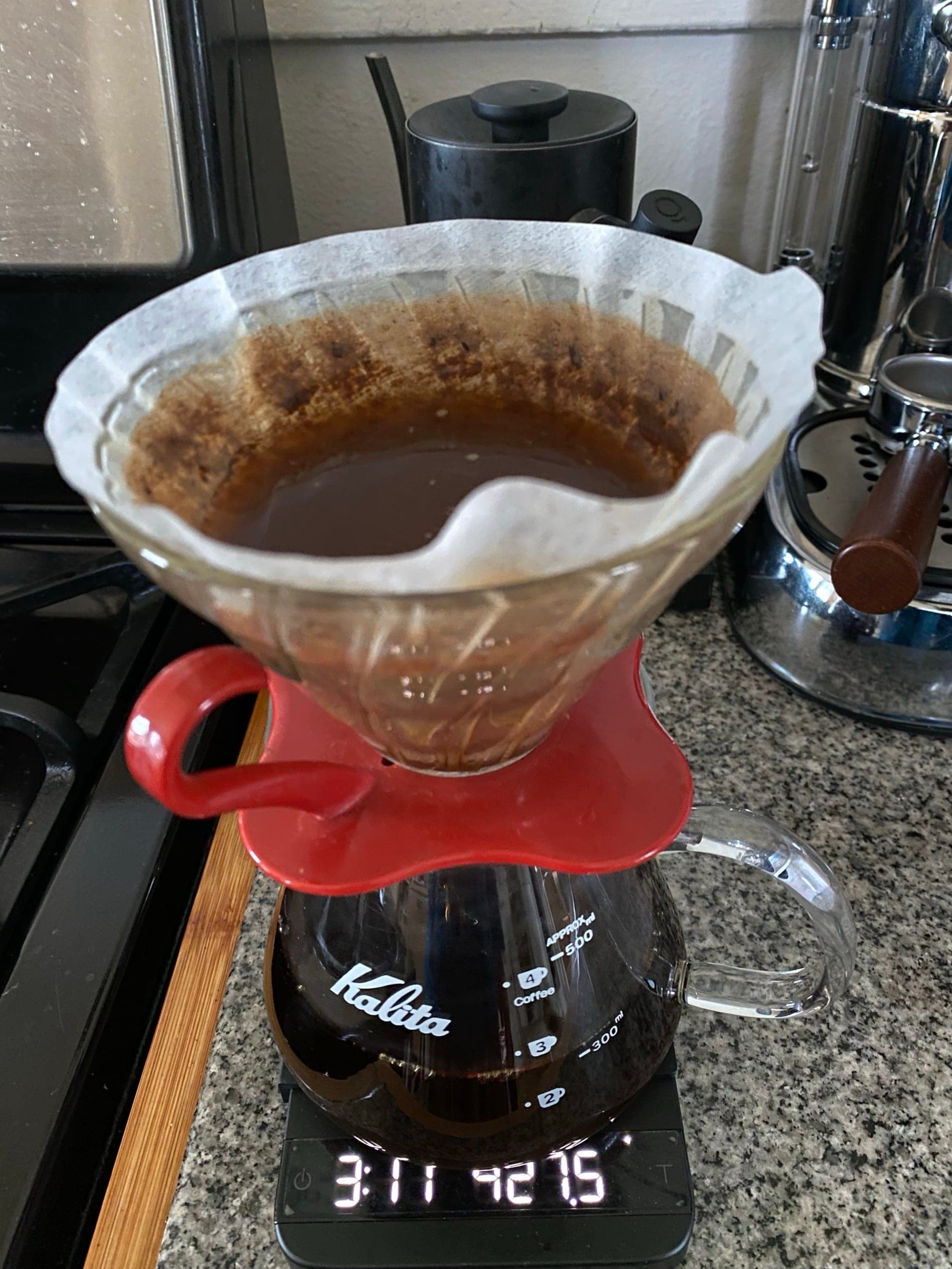 A red Kalita Wave dripper brewing into a glass server on a scale